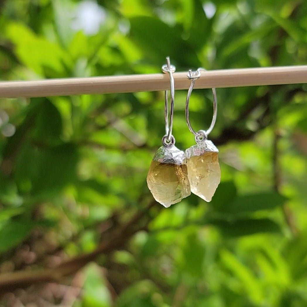 raw citrine silver dangles on hoop earrings in front of green leaves