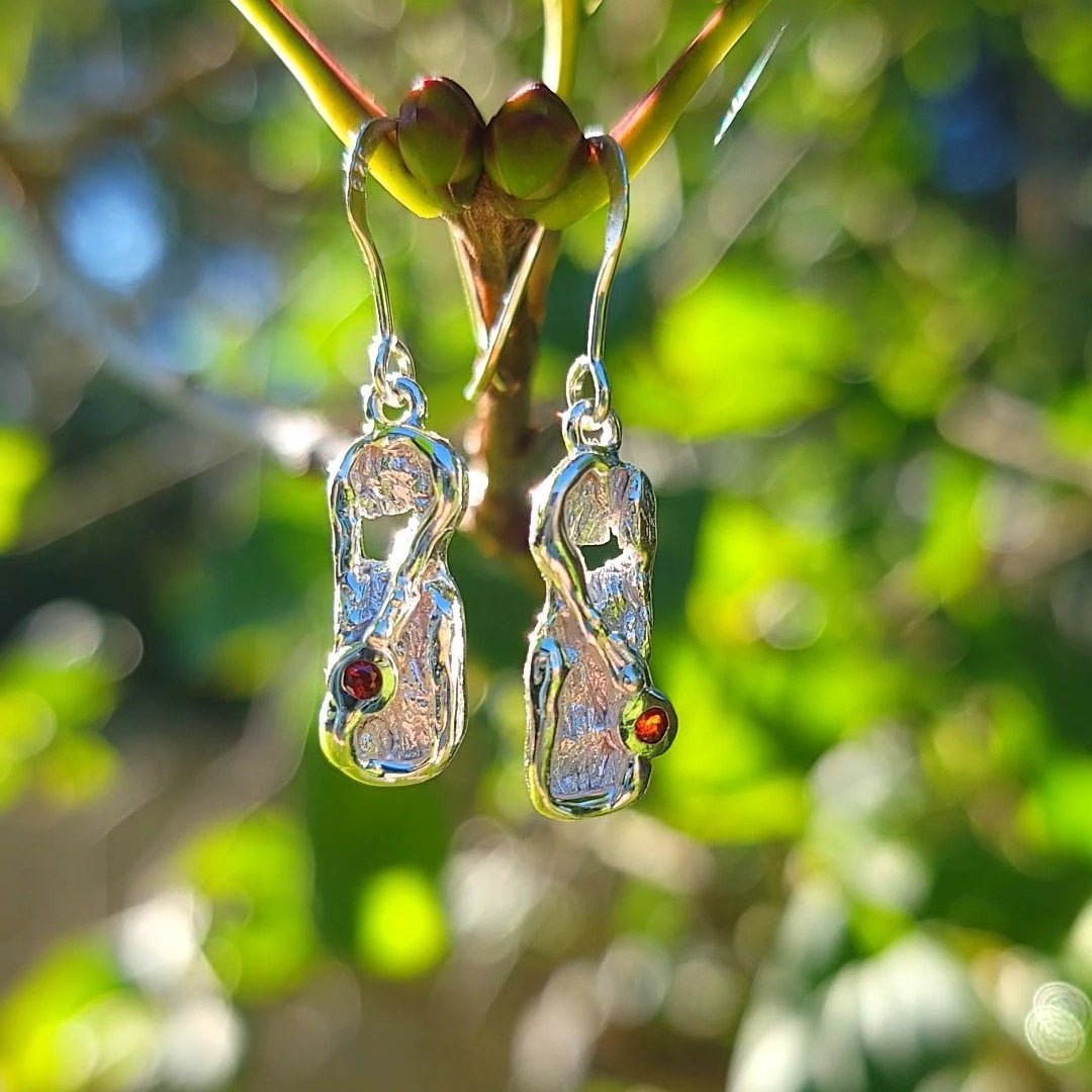 organic  textured garnet and silver dangle earrings lit by the sun in front of greenery