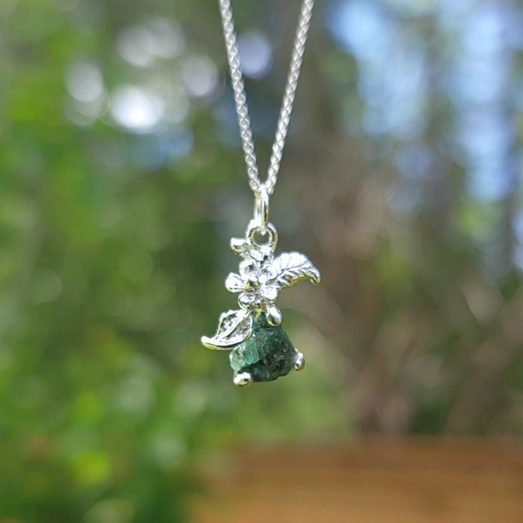 raw emerald stone silver flower pendant necklace in front of trees