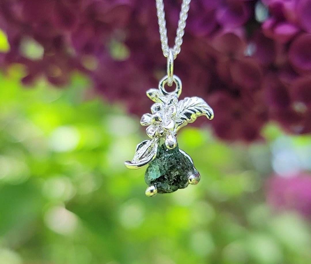 raw natural emerald stone set in silver flower pendant necklace in front of lilacs and grass