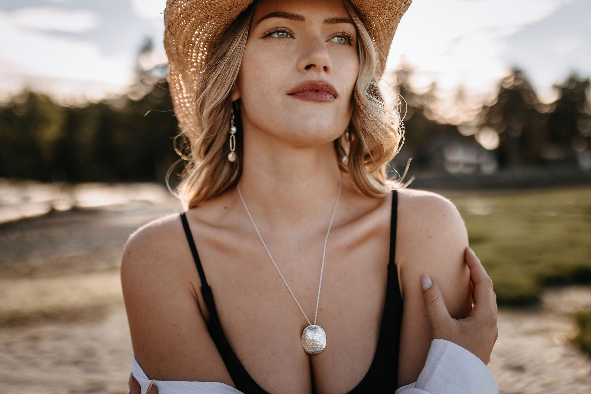 model wearing silver driftwood textured lightweight chandelier statement earrings  and Talia shell necklace with Shop Westvon straw hat