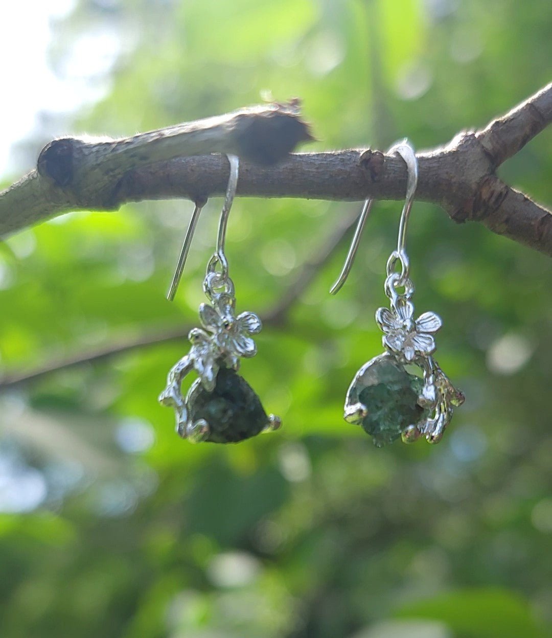  natural raw emerald silver flower earrings hanging from branch outside