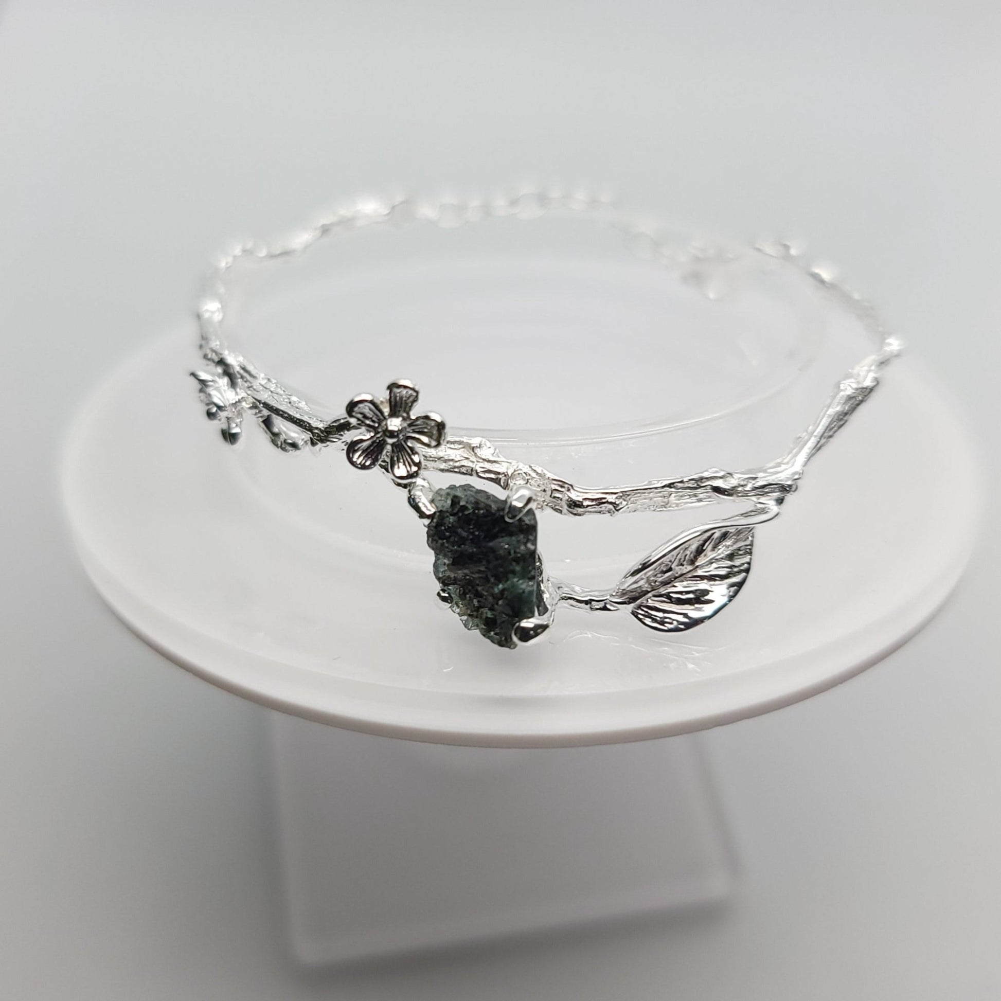 silver branch bracelet adorneds with flowers leaves and a raw emerald centerpiece