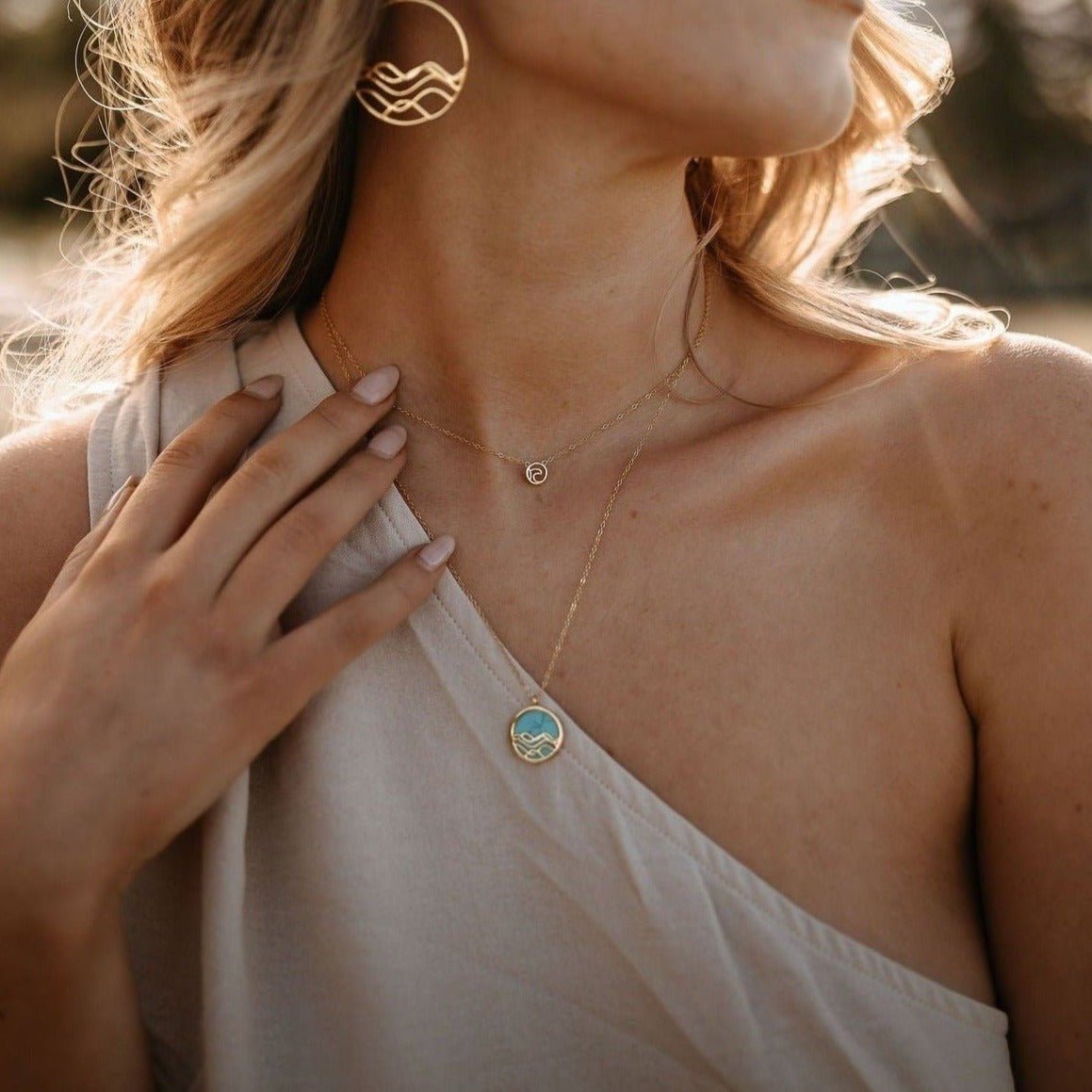 model wearing gold ocean and sea jewelry collection layeres gold and tuquise necklaces and large wave earrings